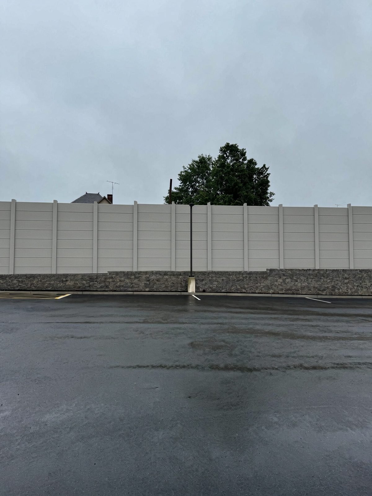 PlywallPRECAST soundwall set on a retaining wall along a parking lot